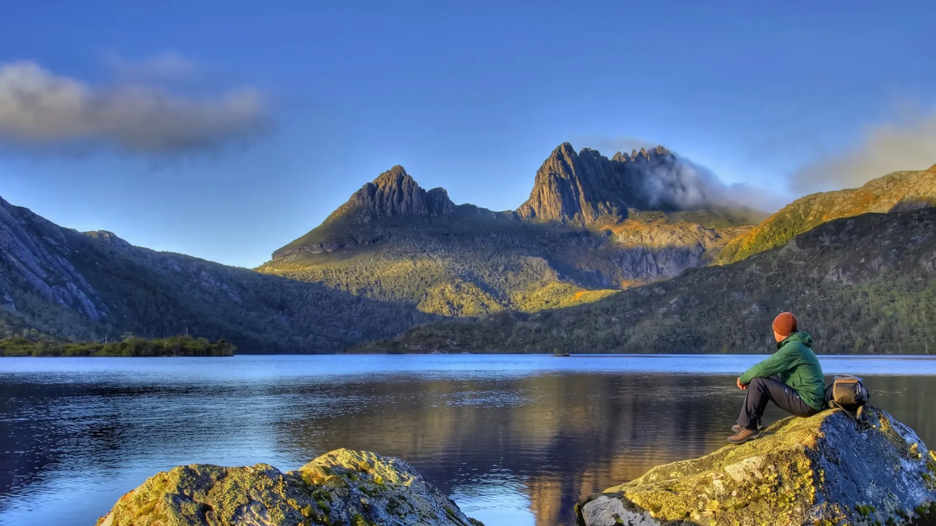 Viaggiatore seduto davanti a un lago della Tasmania con montagne e foreste sullo sfondo